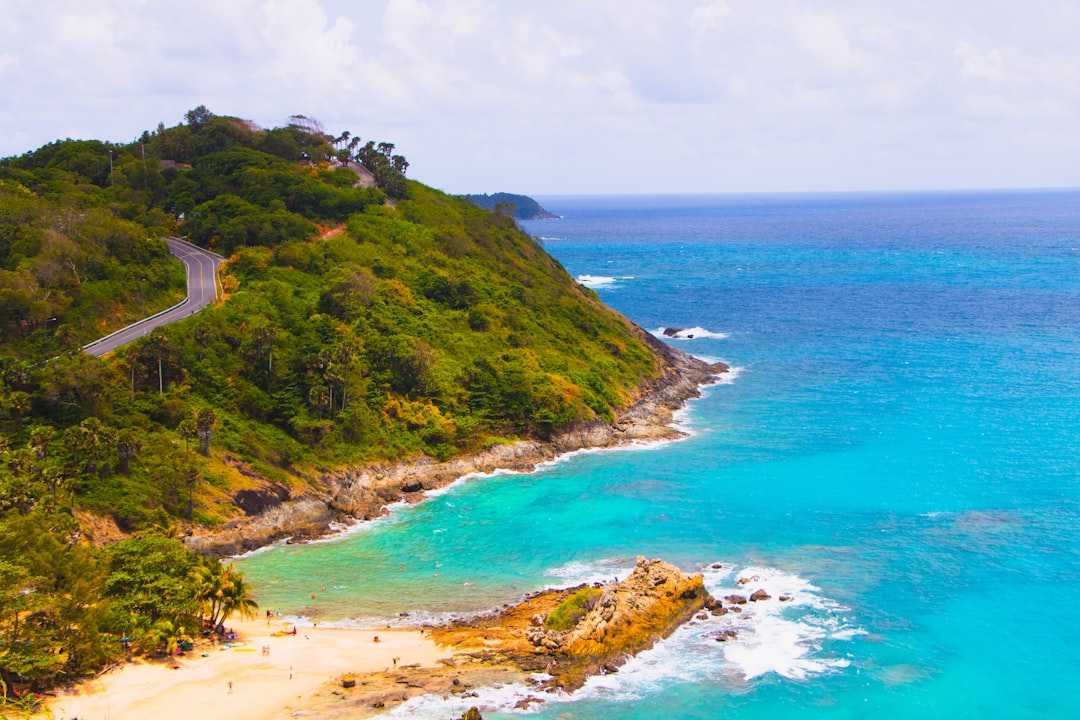 Coastal road winds through lush green hills by turquoise ocean.